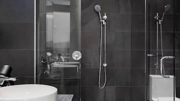 A modern bathroom with a large white sink, a glass shower enclosure, and dark tiled walls.