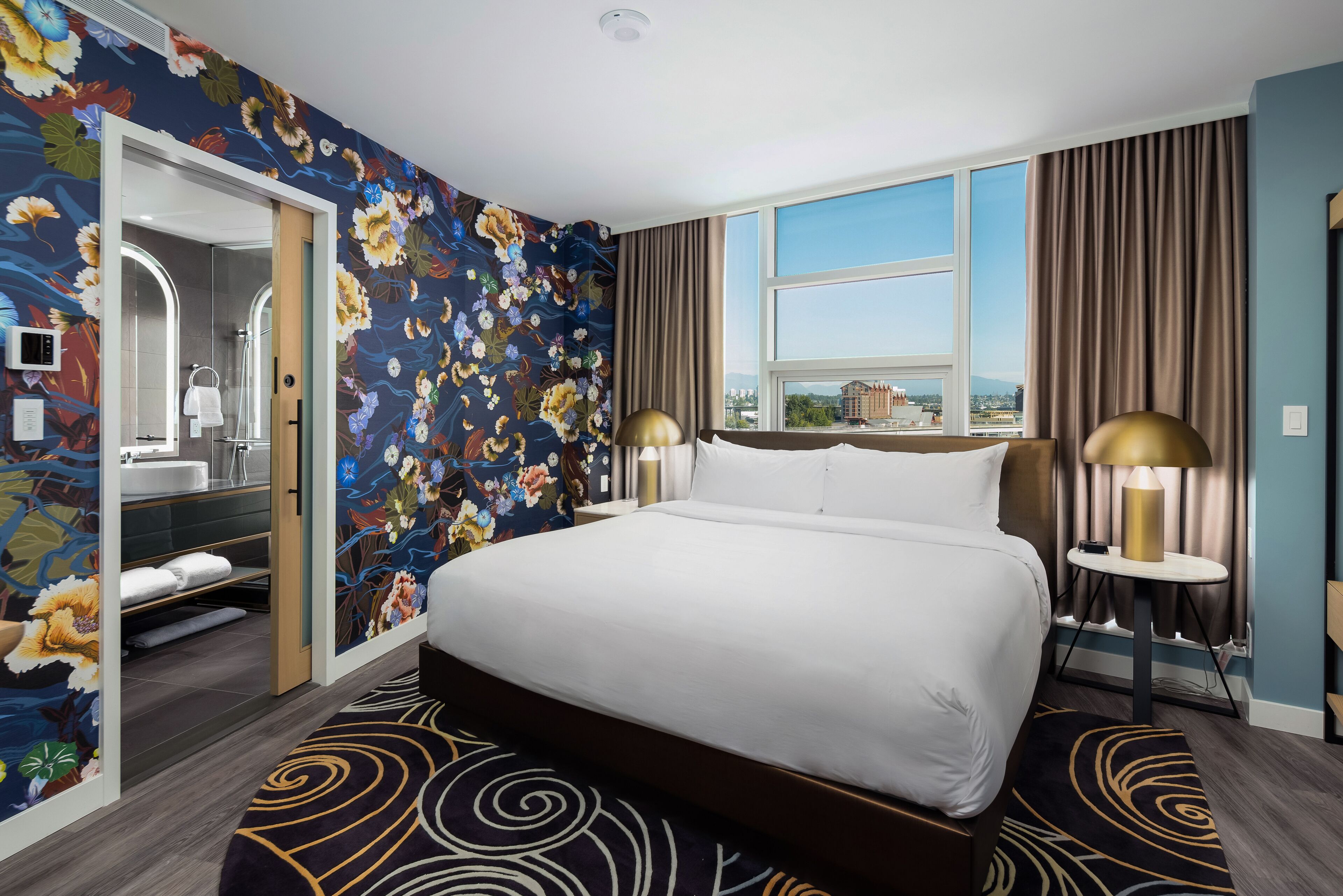 Een hotelkamer met een groot bed, een badkamer met een spiegel en uitzicht op de stad.