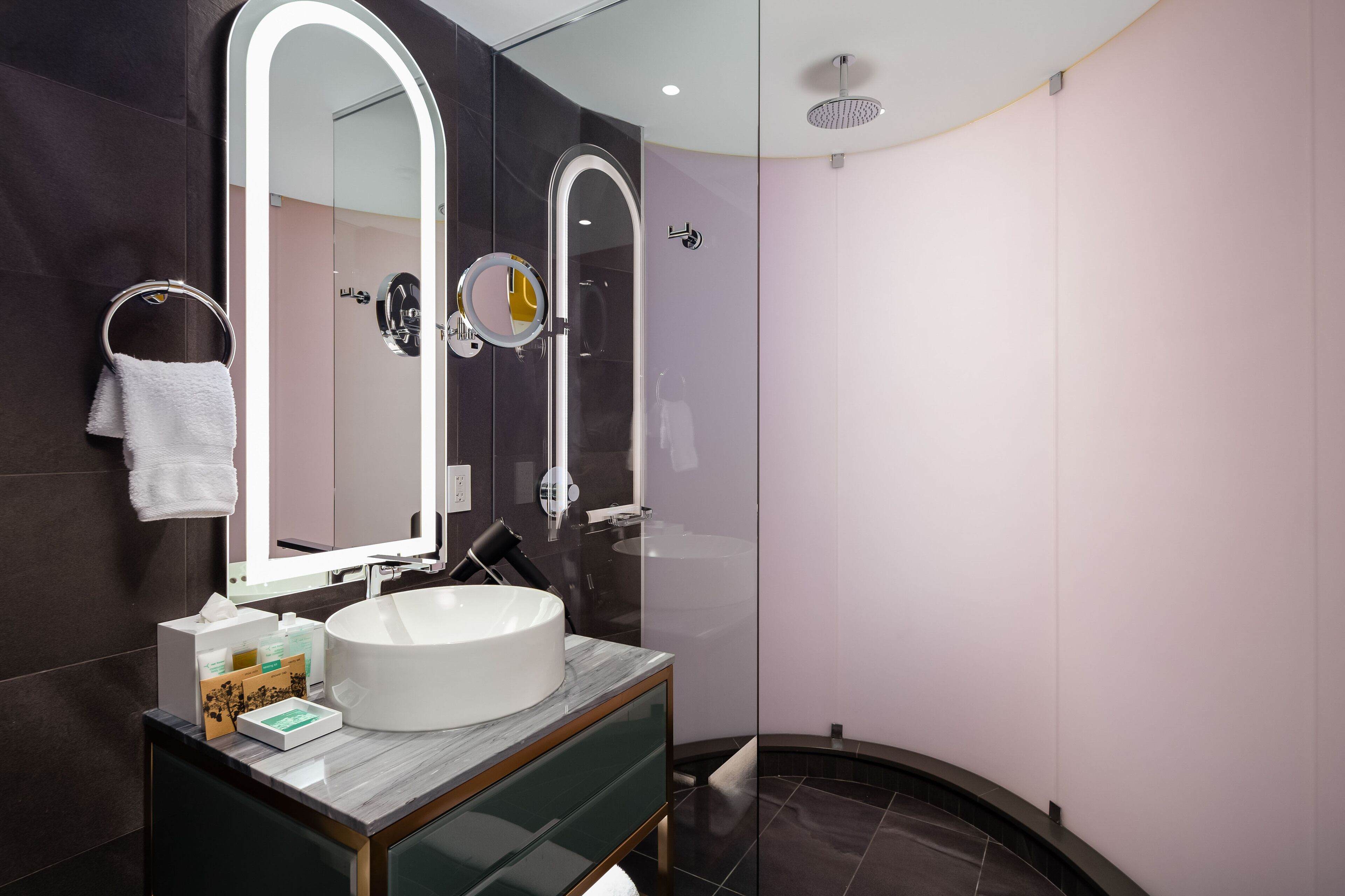 A modern bathroom with a large mirror, a round sink, and a glass shower enclosure.