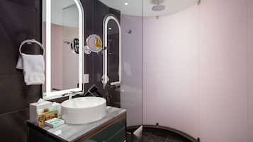 A modern bathroom with a large mirror, a round sink, and a glass shower enclosure.