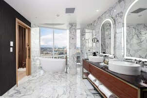 A modern bathroom with a large bathtub, two sinks, and a city view.