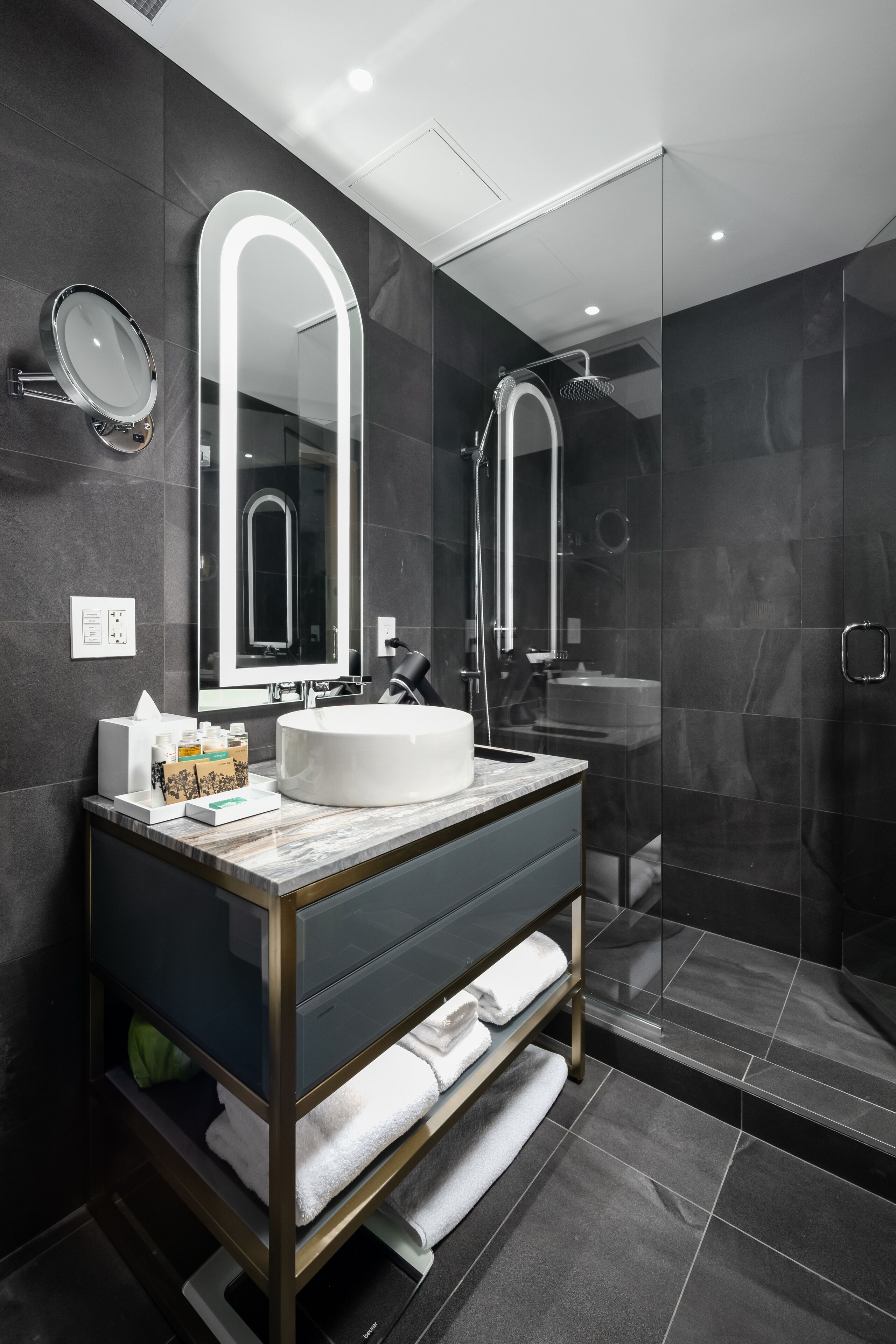 Un baño moderno con un espejo grande, un lavabo redondo y una ducha con mampara de vidrio.