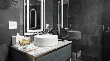 Un baño moderno con un espejo grande, un lavabo redondo y una ducha con mampara de vidrio.