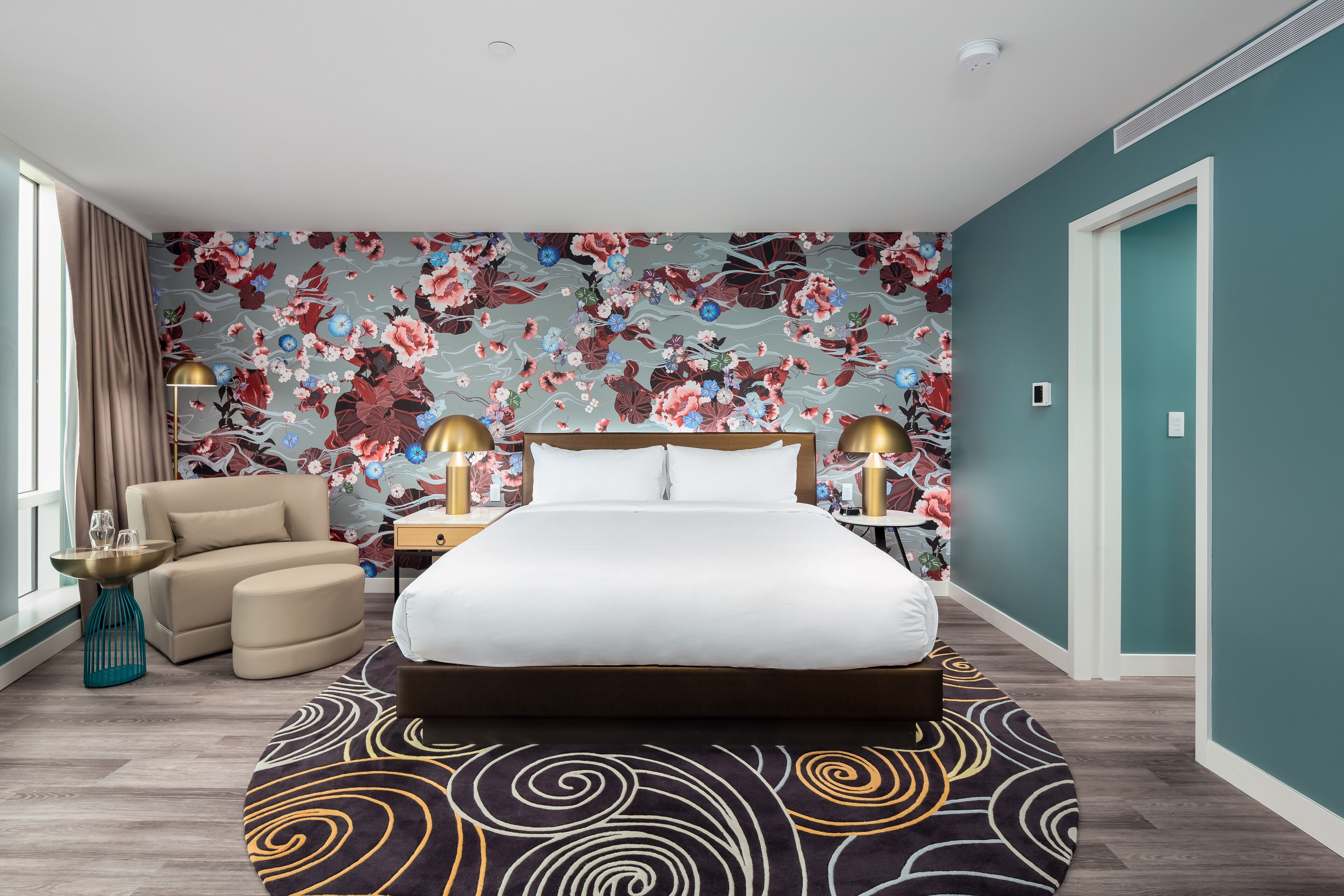 Un dormitorio con una cama grande, una silla, una mesita de noche y un papel tapiz con motivos florales.