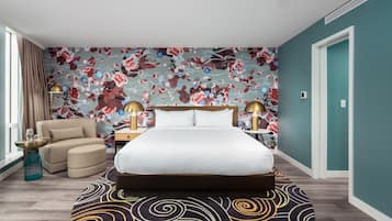 Un dormitorio con una cama grande, una silla, una mesita de noche y un papel tapiz con motivos florales.