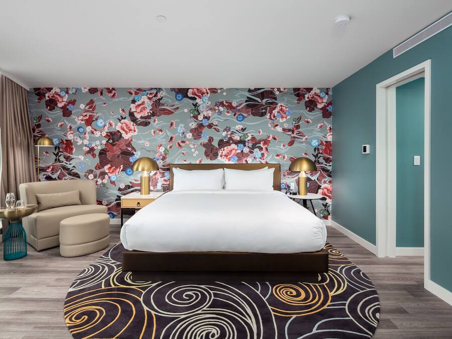 Un dormitorio con una cama grande, una silla, una mesita de noche y un papel tapiz con motivos florales.