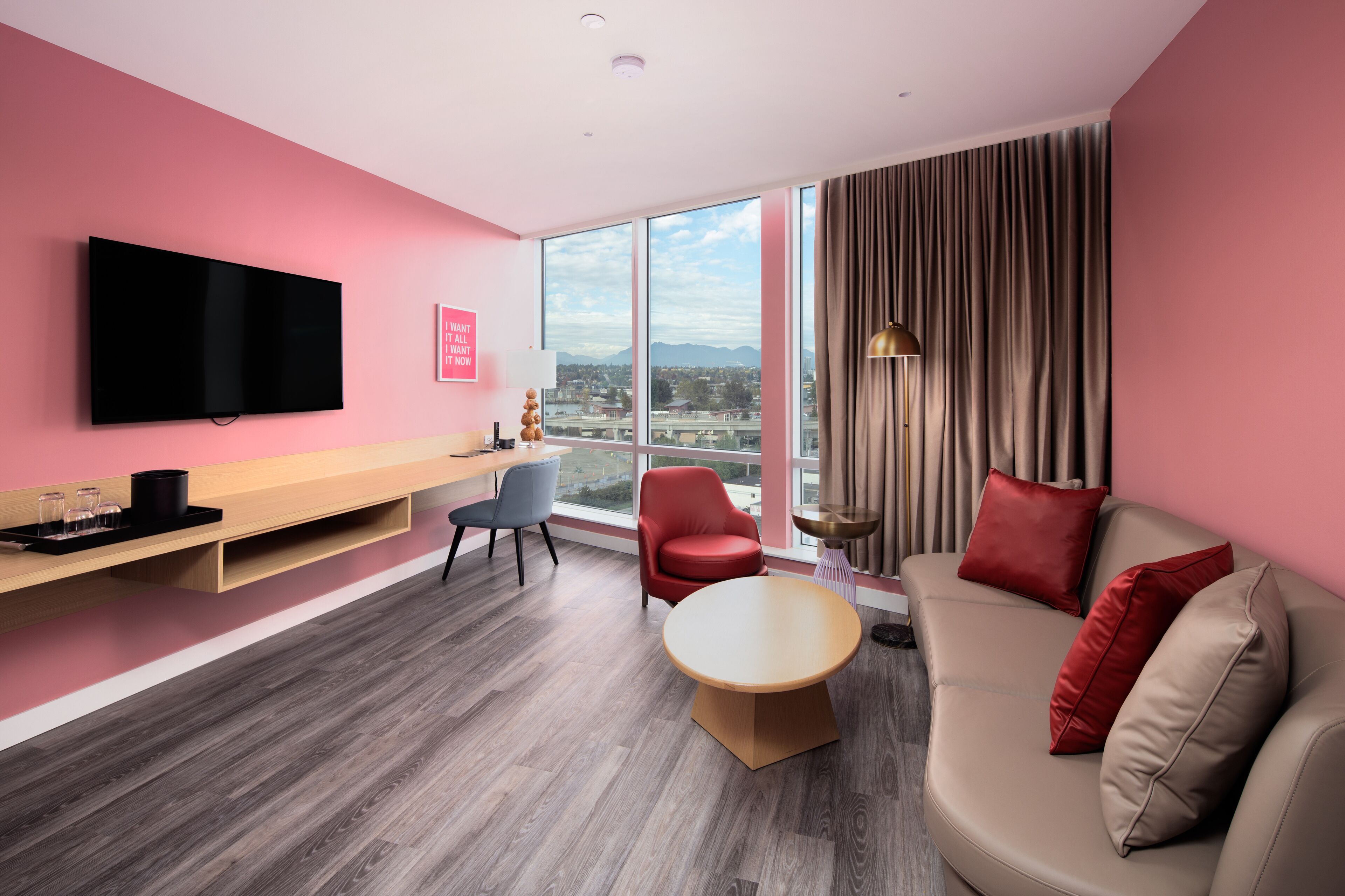 Una habitación de hotel moderna con un ventanal grande, un televisor de pantalla plana, un sofá, una mesa de comedor y una silla.