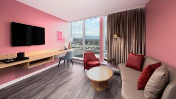 Una habitación de hotel moderna con un ventanal grande, un televisor de pantalla plana, un sofá, una mesa de comedor y una silla.