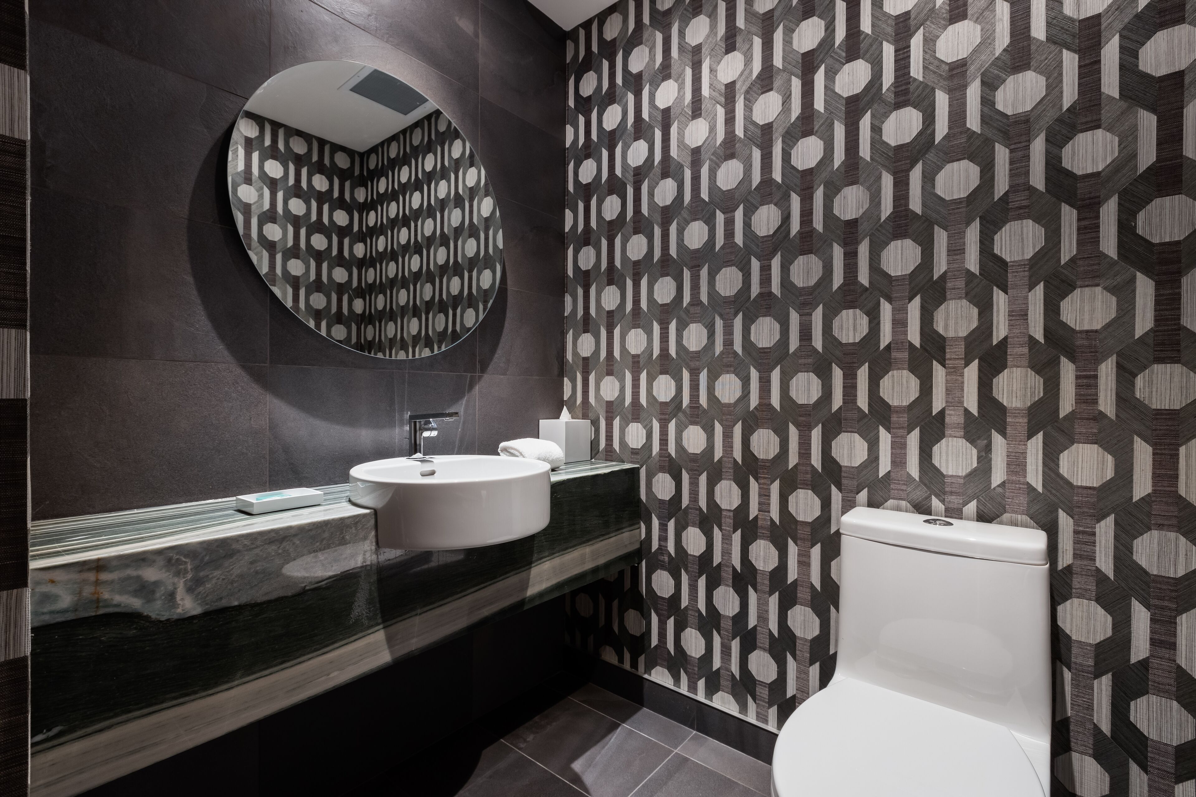 Une salle de bain moderne avec un miroir rond, un lavabo blanc et des toilettes.