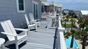 Una terraza de madera con sillas Adirondack blancas, una piscina y vista al océano.