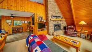 Interior acollidor d'una cabana de fusta amb una llar de foc, parets de fusta, un sofà confortable i una televisió.
