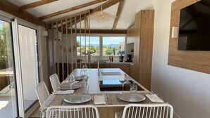 A dining area with a long table set for four, white chairs, and a view of the outdoors through large windows. - Superb house on the ROOF, Terrace with SUPERB VIEW on the CANALS and JACCUZZI (Grimaud)