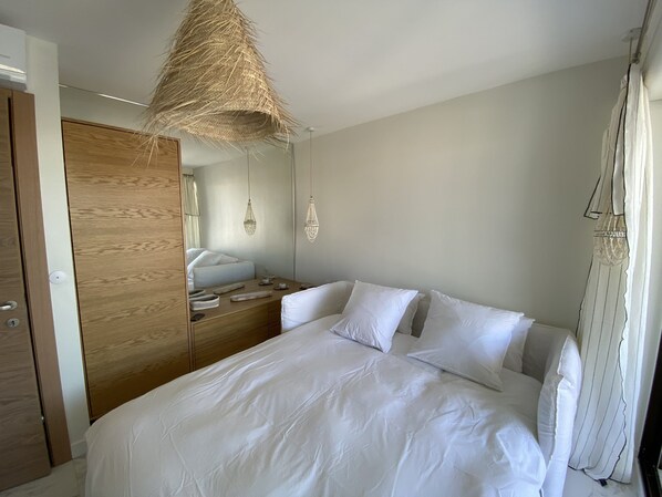 A bedroom with a bed, wooden wardrobe, bedside table, and hanging light fixture. - Superb house on the ROOF, Terrace with SUPERB VIEW on the CANALS and JACCUZZI (Grimaud)