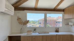 A kitchen with wooden cabinets, a window with a view of buildings, and a white countertop. - Superb house on the ROOF, Terrace with SUPERB VIEW on the CANALS and JACCUZZI (Grimaud)
