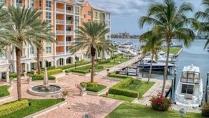 Een meerhoog hotel met balkons, een jachthaven met boten en palmbomen.