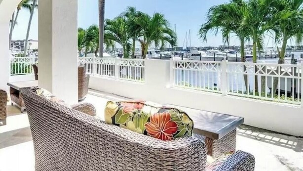 Een overdekt terras met rieten meubels en uitzicht op een jachthaven met boten en palmbomen.