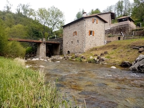 Un bâtiment en pierre avec un pont enjambant un ruisseau, le tout entouré de verdure.