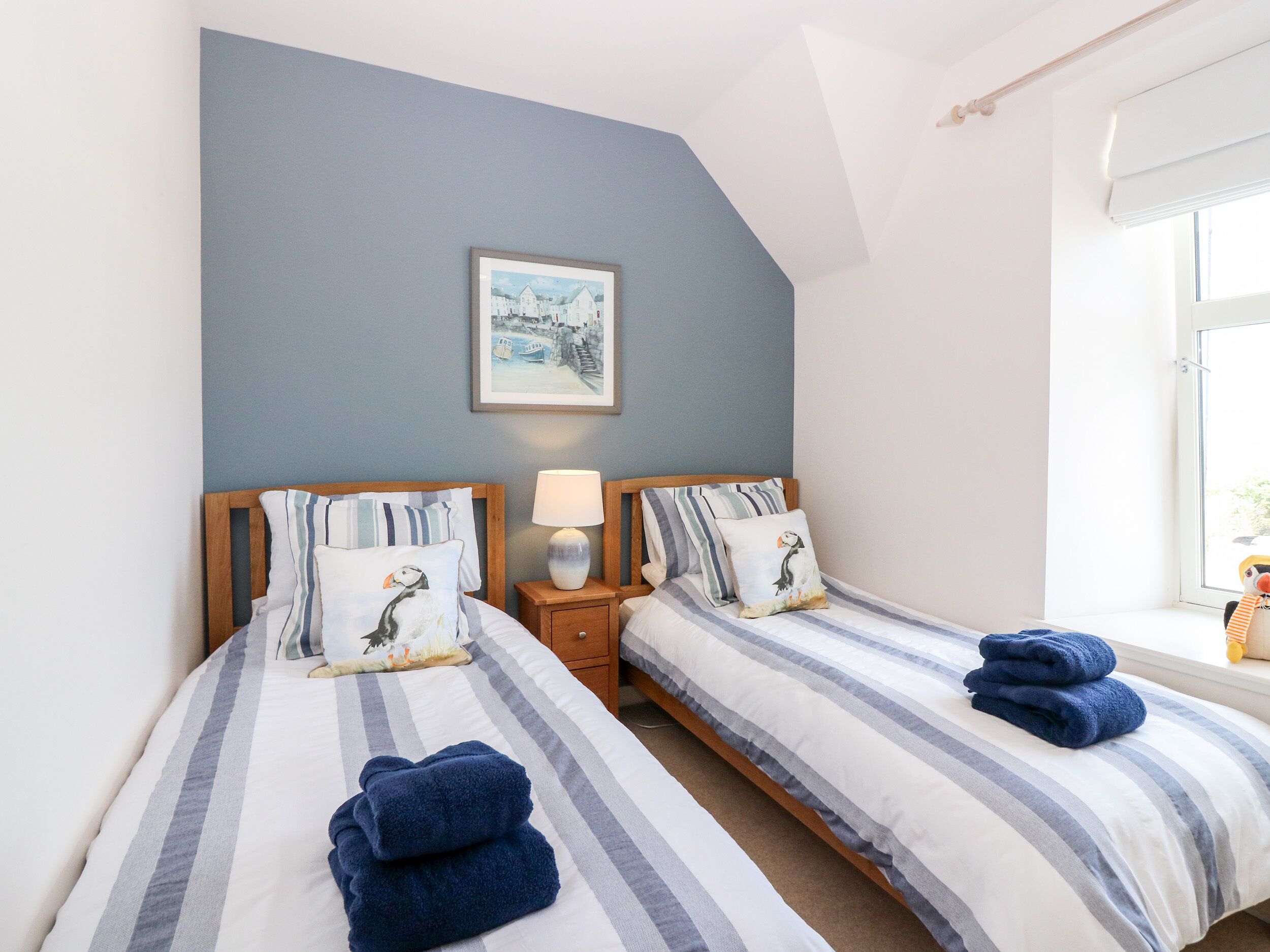 Une chambre à coucher avec deux lits, chacun doté de draps à rayures et d’oreillers assortis, d’une lampe de chevet et d’un tableau encadré au mur.