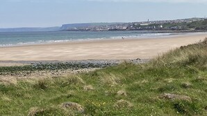 Una playa costera con un primer plano rocoso, una playa de arena y un pueblo al fondo.