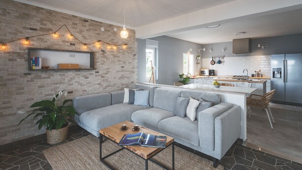 Un salon moderne avec un canapé gris, une table basse sur laquelle sont posés des magazines et un mur en briques décoré de guirlandes lumineuses.