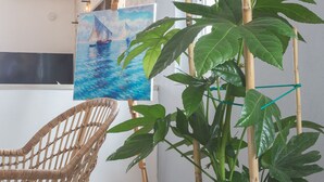 Une pièce avec une grande plante en pot, une chaise en osier et un tableau représentant un voilier accroché au mur.