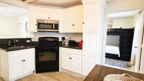 Une cuisine de taille réduite avec des meubles blancs, une cuisinière noire, un four à micro-ondes et une machine à café.