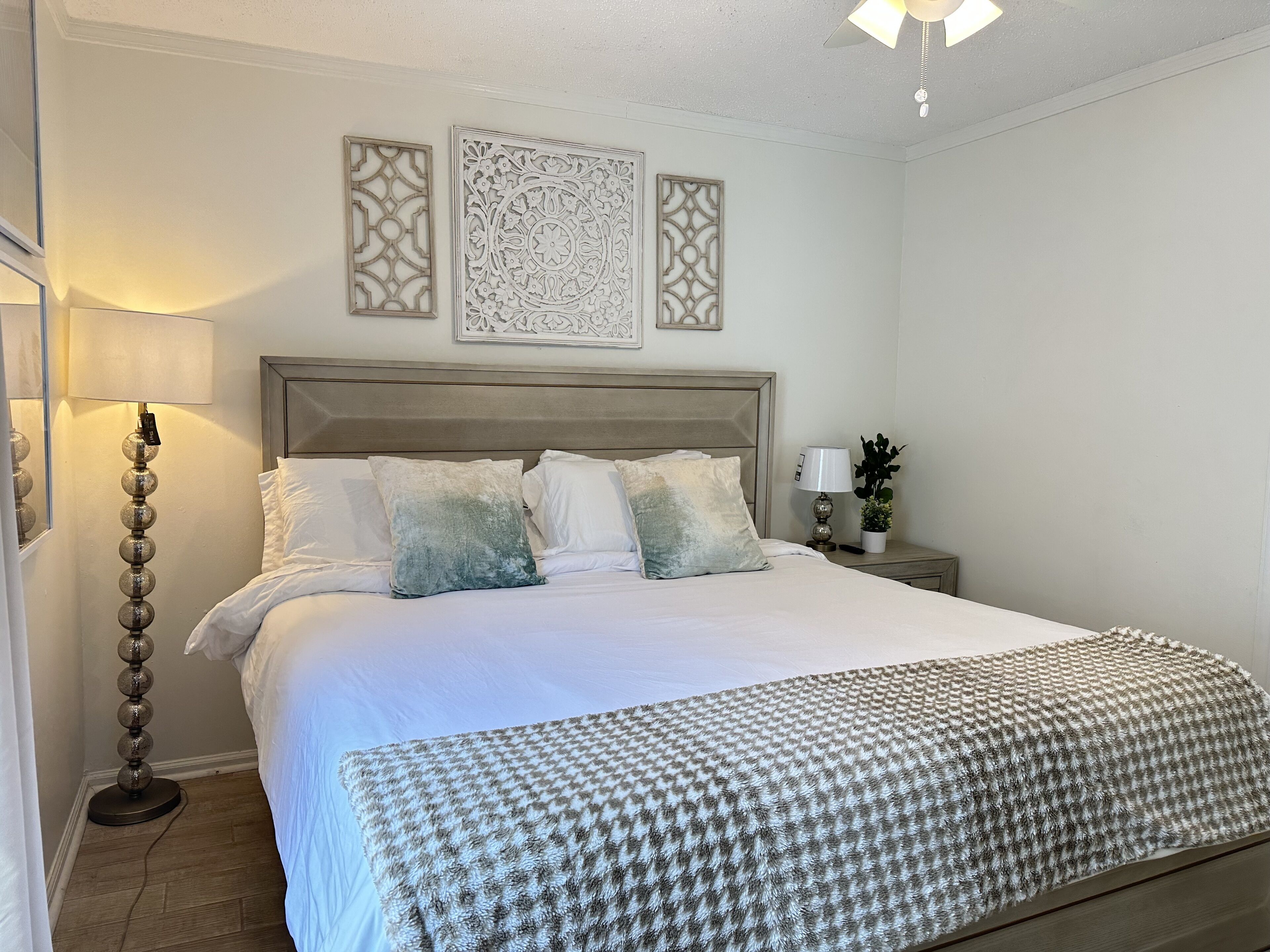 A neatly made bed with a patterned throw, a bedside lamp, and decorative wall art.