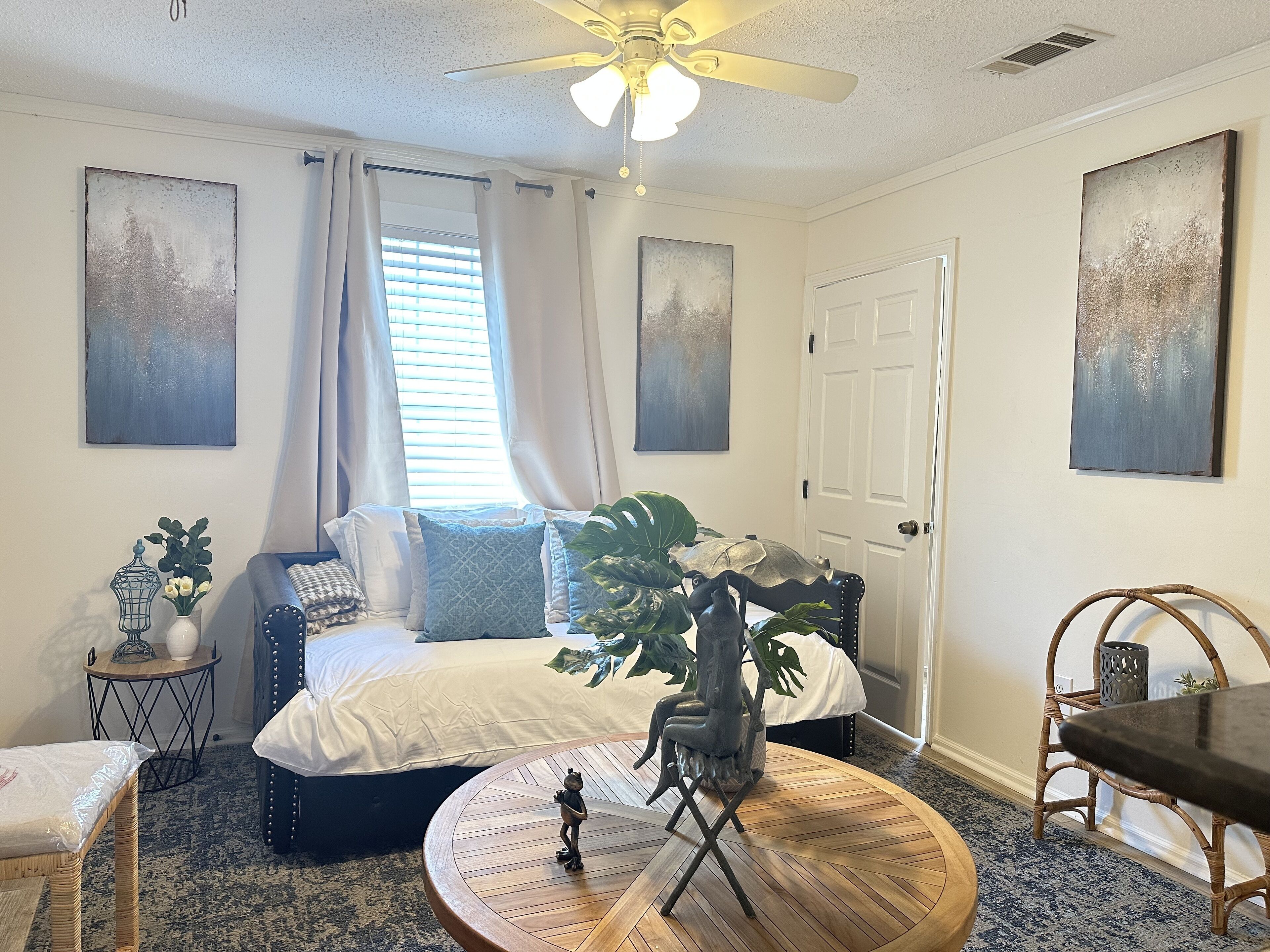 Une chambre à coucher avec un lit, une table ronde en bois, une chaise, une petite table d’appoint et deux tableaux accrochés aux murs.