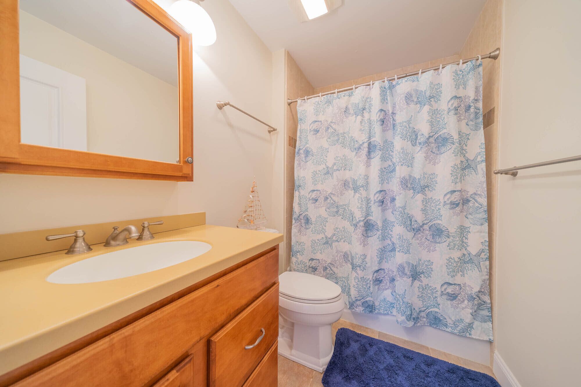 A bathroom with a wooden vanity, a white sink, a toilet, and a shower curtain with a floral pattern.