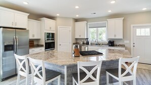 A modern kitchen with white cabinetry, a stainless steel refrigerator, an island with seating, and built-in appliances. - Beautiful Home, Ocean Views, Block from Ocean, within 5mi of 7 Golf Courses,   (North Myrtle Beach)