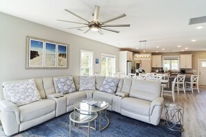 A spacious living room with a sectional sofa, a glass coffee table, and a ceiling fan.