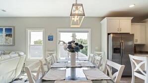 Een eethoek met een glazen tafel, witte stoelen, een vaas met bloemen en een hanglamp.