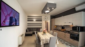 A modern kitchen with a dining area, a TV mounted on the wall, and a clock. - Casa A&F - Fra (Torricella)