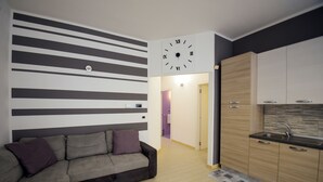 A modern living room with a sofa and a kitchen area with wooden cabinets and a sink. - Casa A&F - Fra (Torricella)