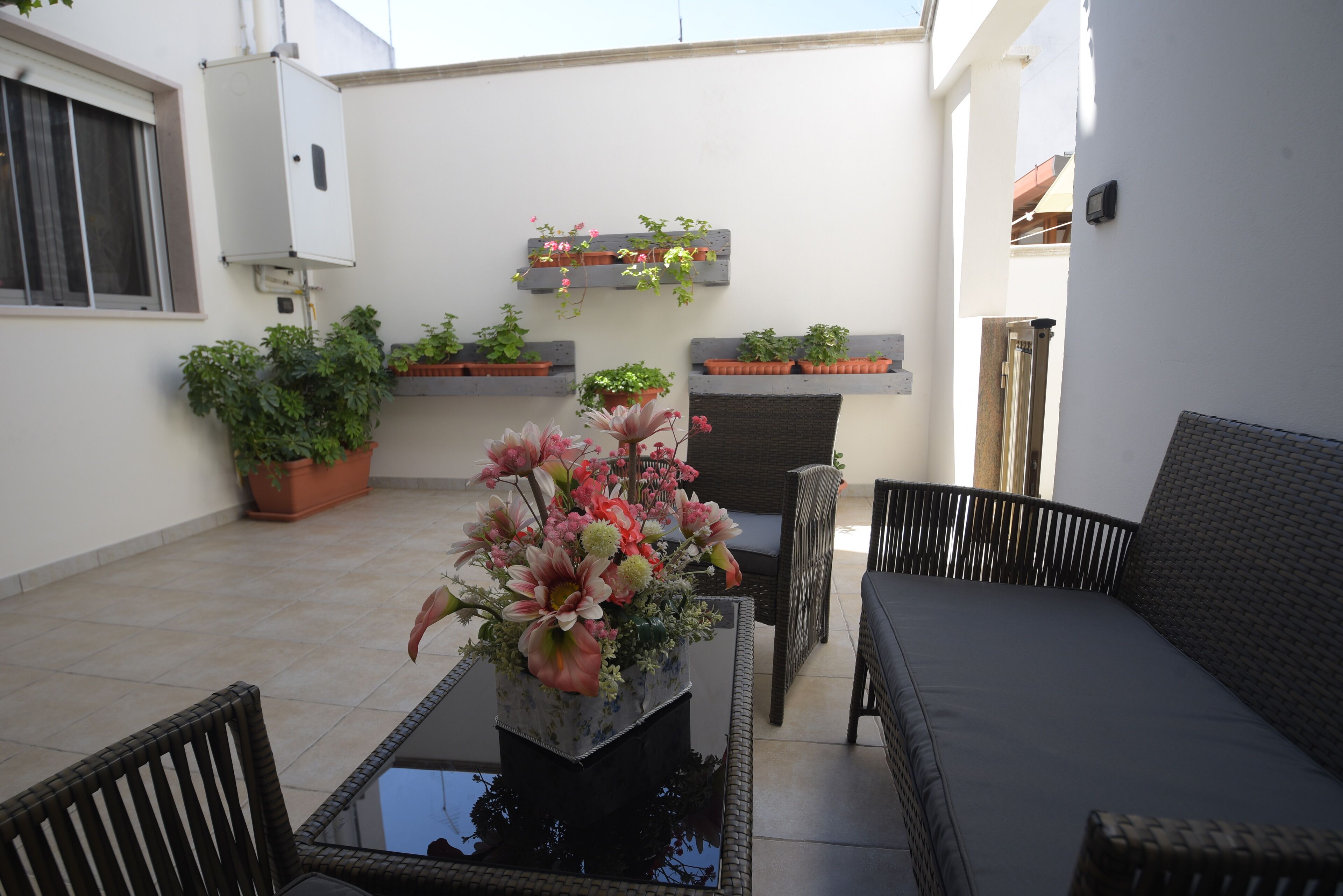 Eine Terrasse mit Glastisch, Korbstühlen und Topfpflanzen.