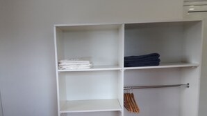 Armadio a muro con scaffali multipli e spazio per appendere, un tavolino con un oggetto rosso e un letto con copriletto arancione.