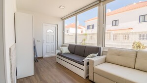 A room with a sofa, a small table, a door, and a window with a view of buildings.