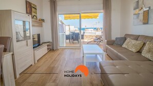 A modern living room with a sofa, a coffee table, and a TV. There is a sliding glass door leading to an outdoor area with a yellow umbrella. - #057 T1 Rossio 43D by Home Holidays (Albufeira)