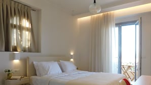 A bedroom with a bed, bedside table, lamp, and a view of the outdoors. - Orea Superior Rooms (Zakynthos)
