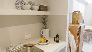 A kitchen with a stainless steel sink, white countertops, a white vase with dried plants, a coffee maker, and a plate of lemons. - Orea Superior Rooms (Zakynthos)