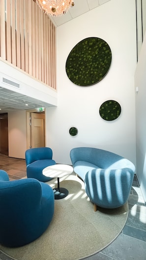 Recepció moderna amb seients blaus, una taula rodona i una gran obra d'art circular de color verd a la paret.