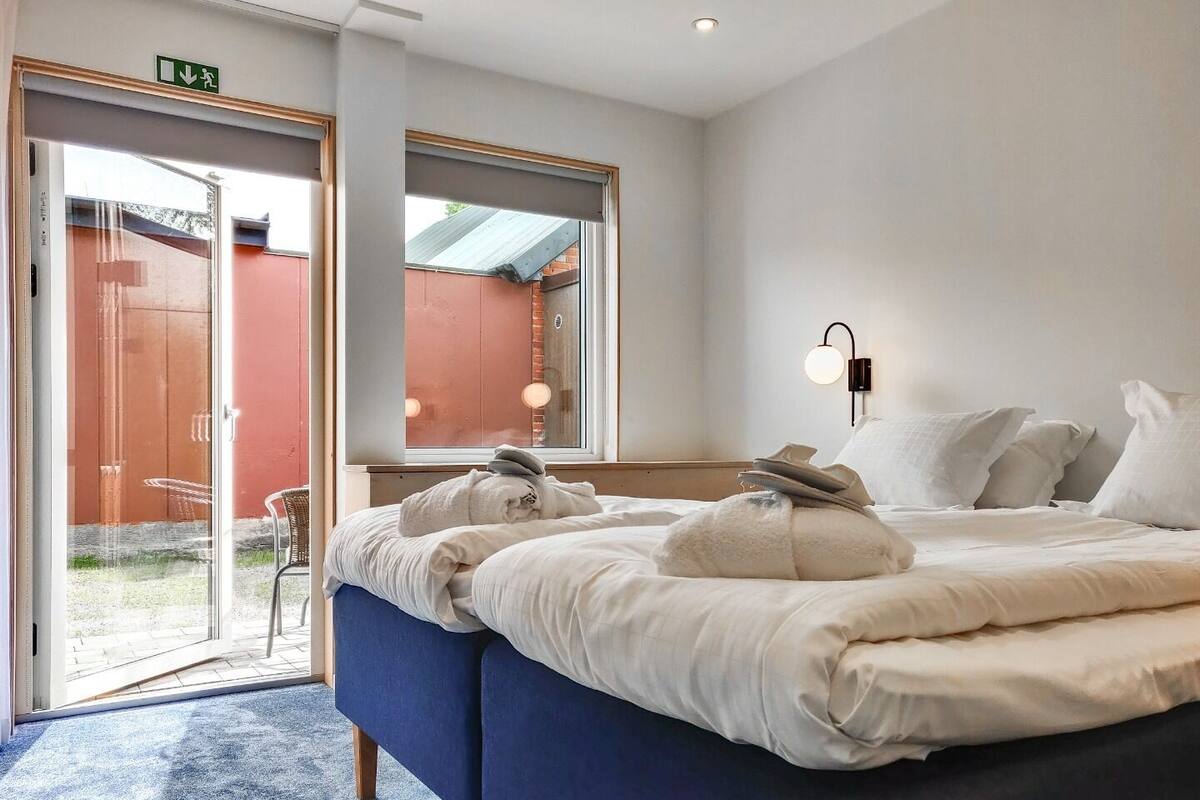 A hotel room with a bed, a window, and a door leading to an outdoor area.