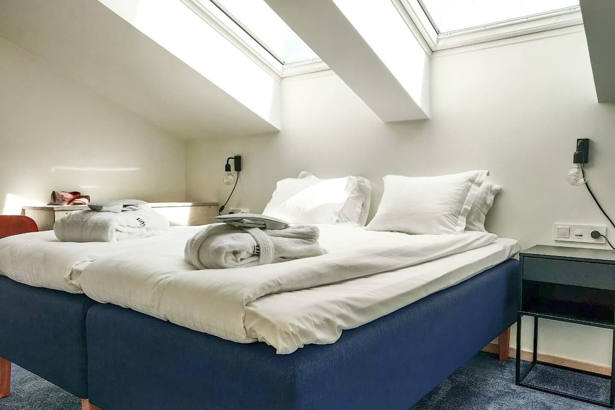 A hotel room with a large bed, a desk, and a chair. There is a skylight above the bed.