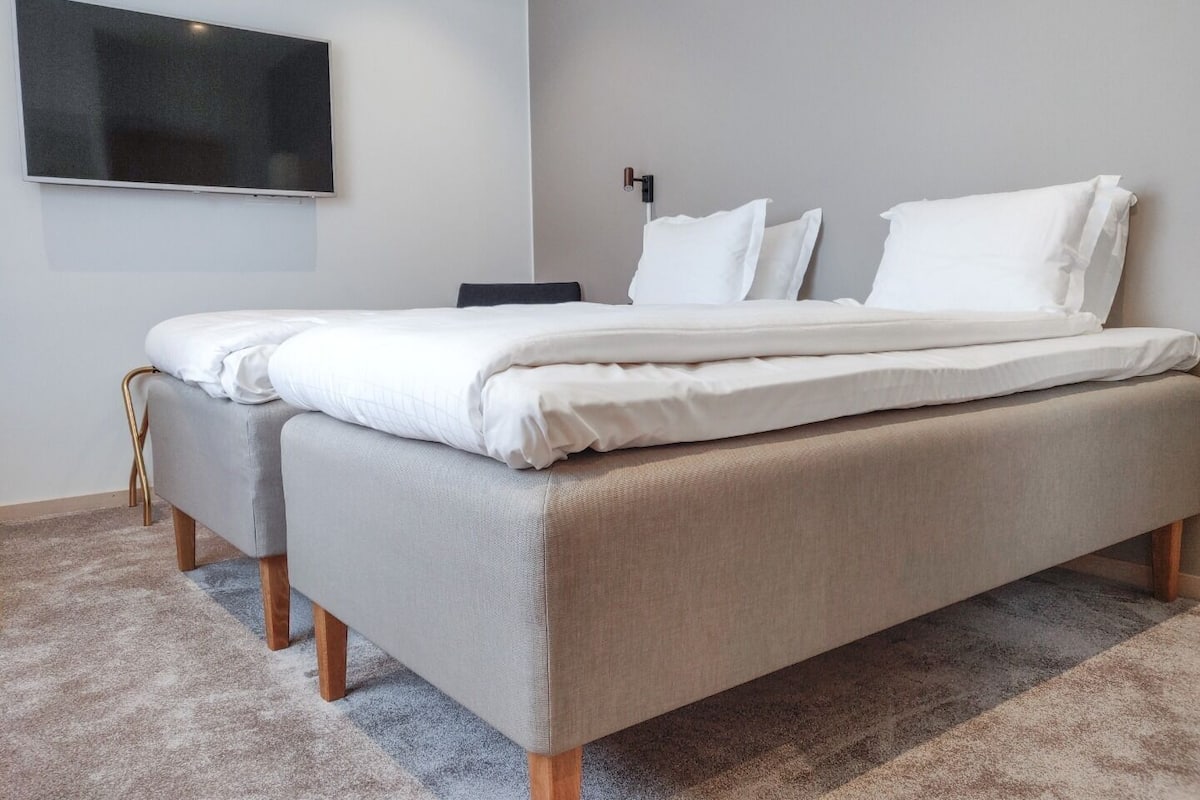 A modern bedroom with a bed, a flat-screen TV mounted on the wall, and a bedside table.