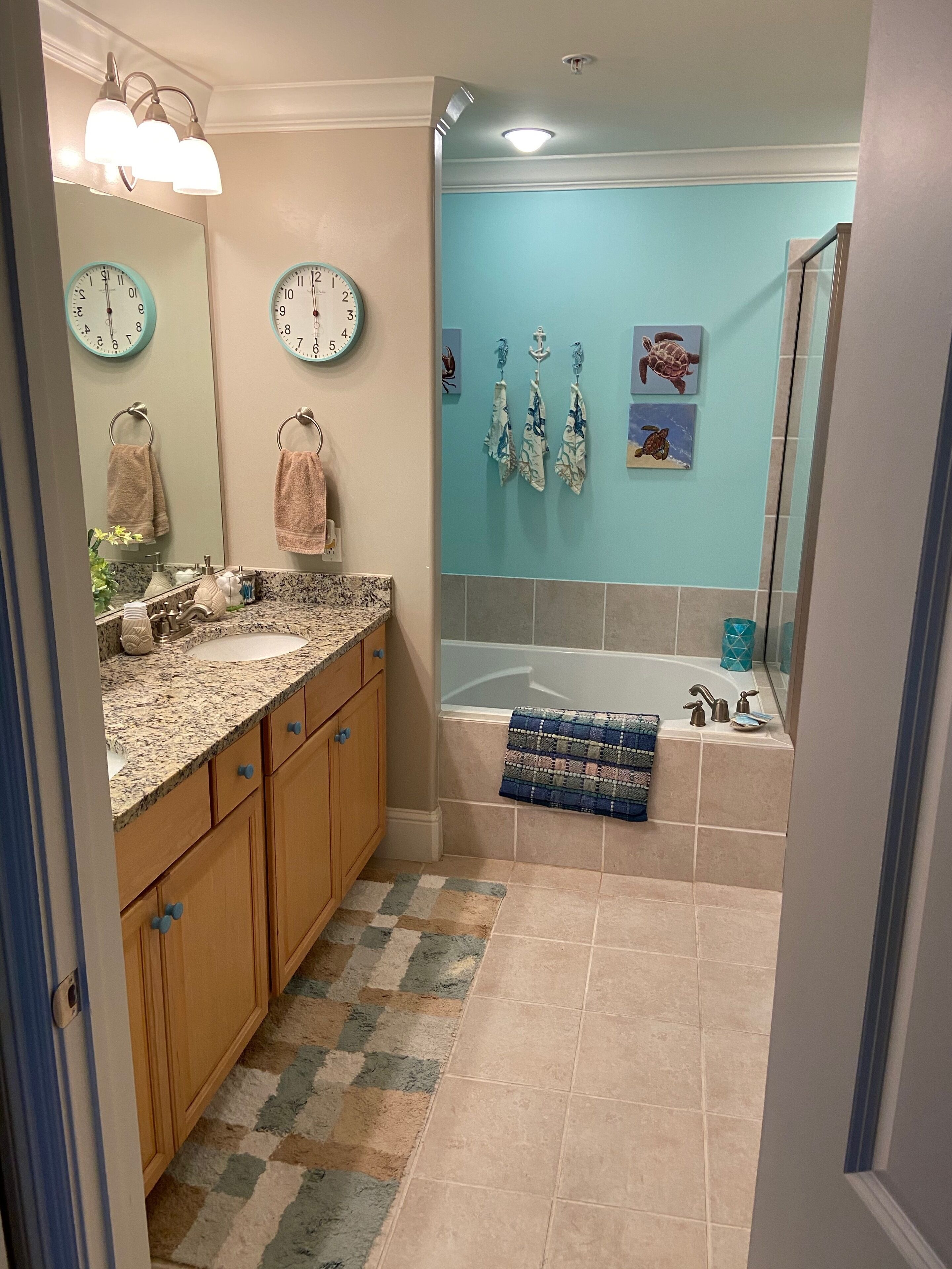 A bathroom with a sink, mirror, towel rack, clock, and a bathtub with a shower curtain.