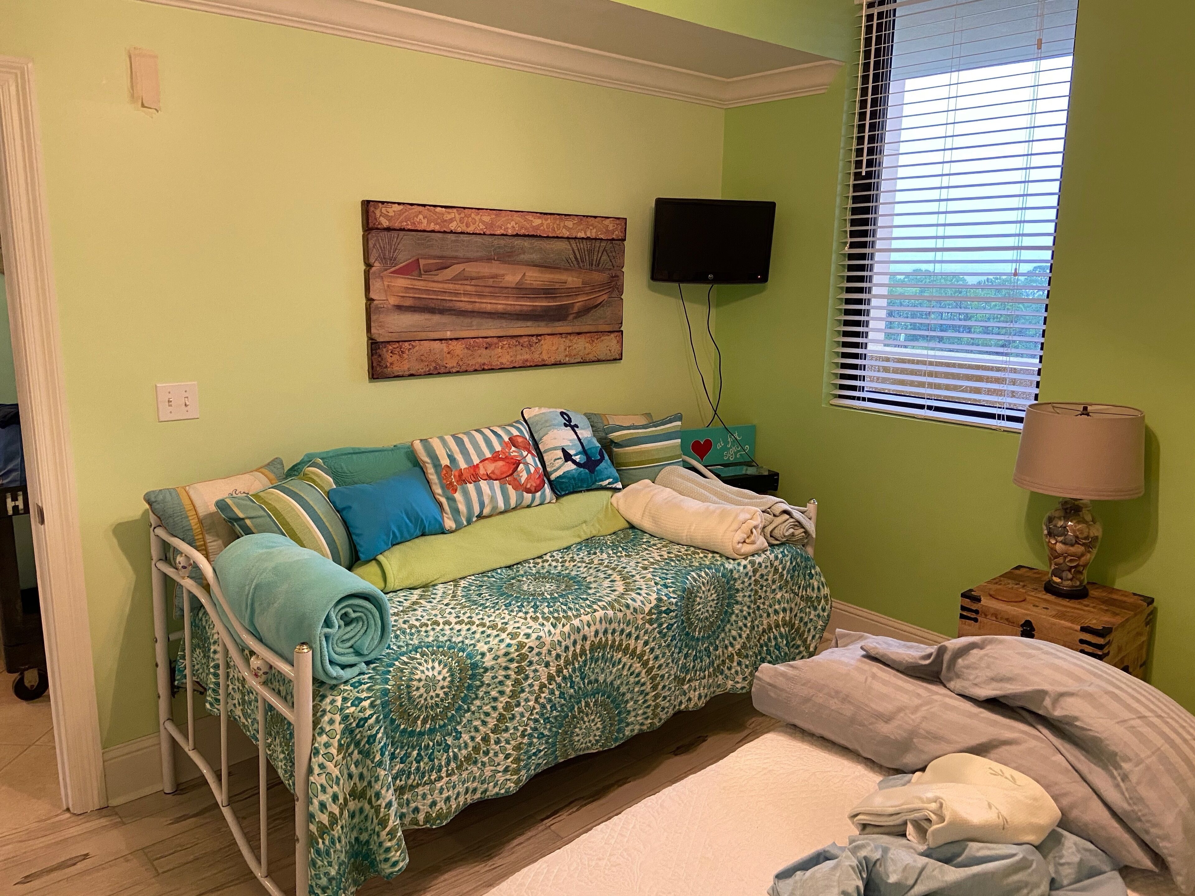 A cozy bedroom with a bed, a sofa bed, a TV, and a lamp.
