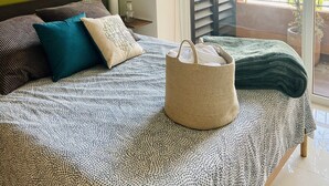 Een slaapkamer met een bed, een macramé wanddecoratie, een grote geweven tas en uitzicht buiten via een schuifdeur.