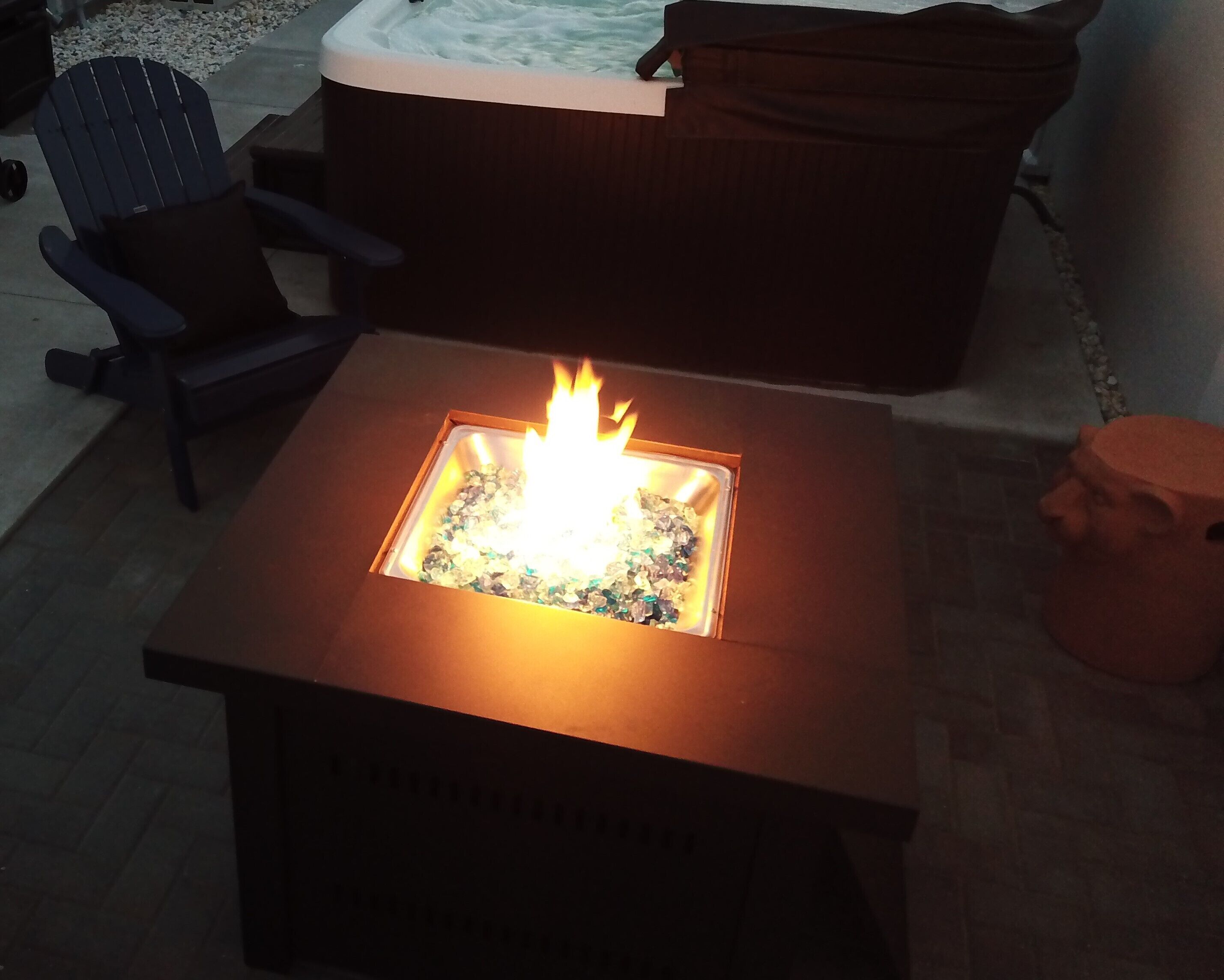 A square fire pit with a visible flame, surrounded by a wooden base.