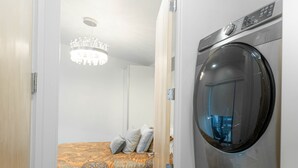 Een compacte slaapkamer met een bed, een wasmachine en een kroonluchter.