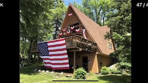 A wooden cabin with a large American flag, surrounded by trees. - ‘Not To Worry’ Waterfront Home (Wolcott)